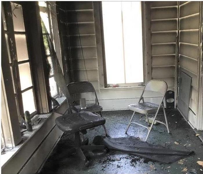 Soot covered walls and two chairs with fire damage in a room.