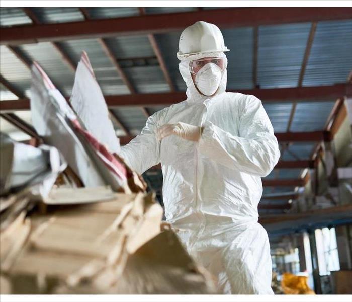 Low angle portrait of factory worker wearing biohazard suit sorting reusable cardboard on waste processing plant